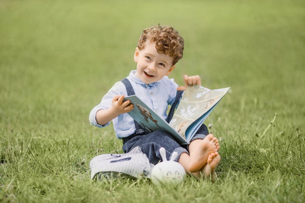 En enfant pieds nus sur l'herbe qui vit le présent, riant avec un livre à la main.