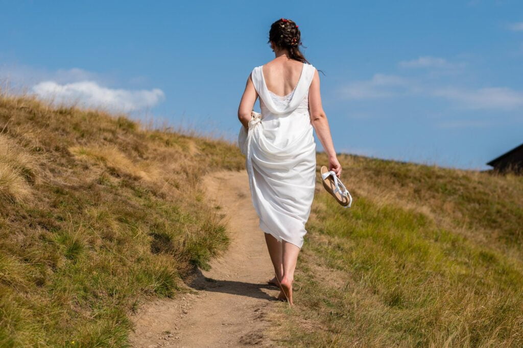 Une femme qui marche pieds nus en robe blanche sur un chemin de campagne.