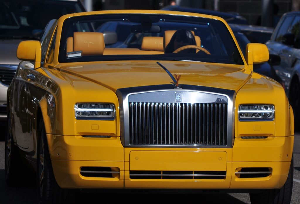 Une voiture rolls royce jaune décapotable conduite par une femme qui s'est posée la question "Comment l'obtenir la voiture que je veux ?"