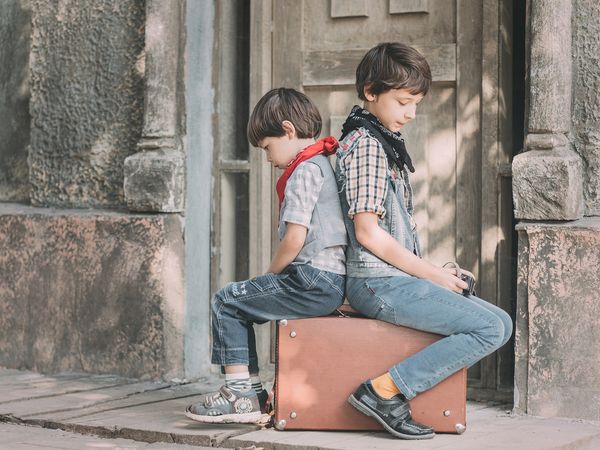 2 garçons qui sont dos à dos assis sur des valises, peut-être se détestent-ils comme moi avec cette femme ?